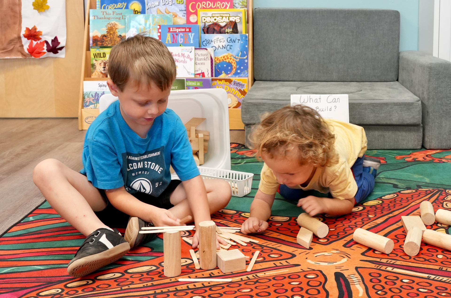 Two children building with wooden blocks on a colorful rug in a playroom