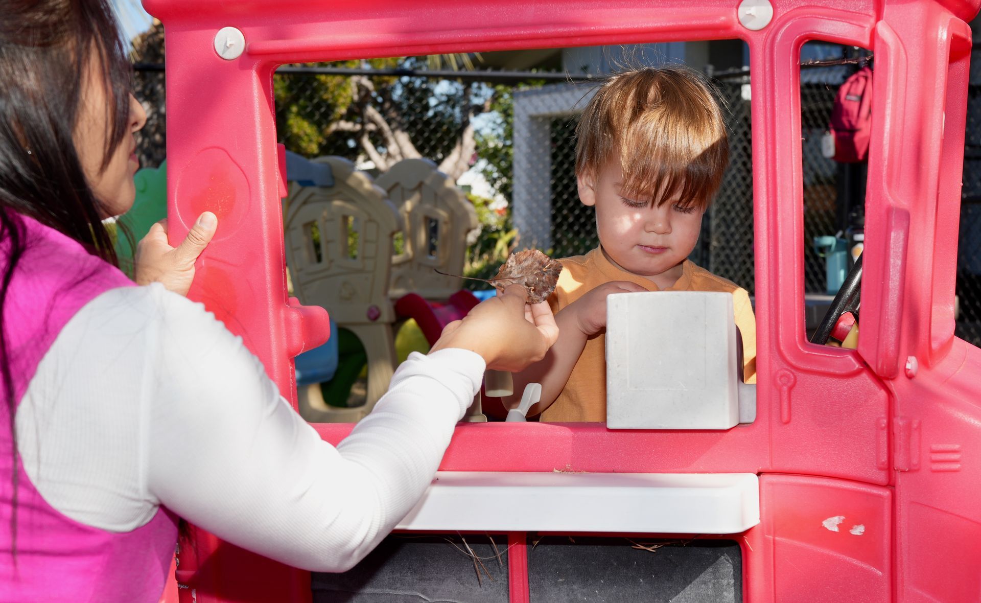 Child at a pink playhouse window handing an item to an adult outside