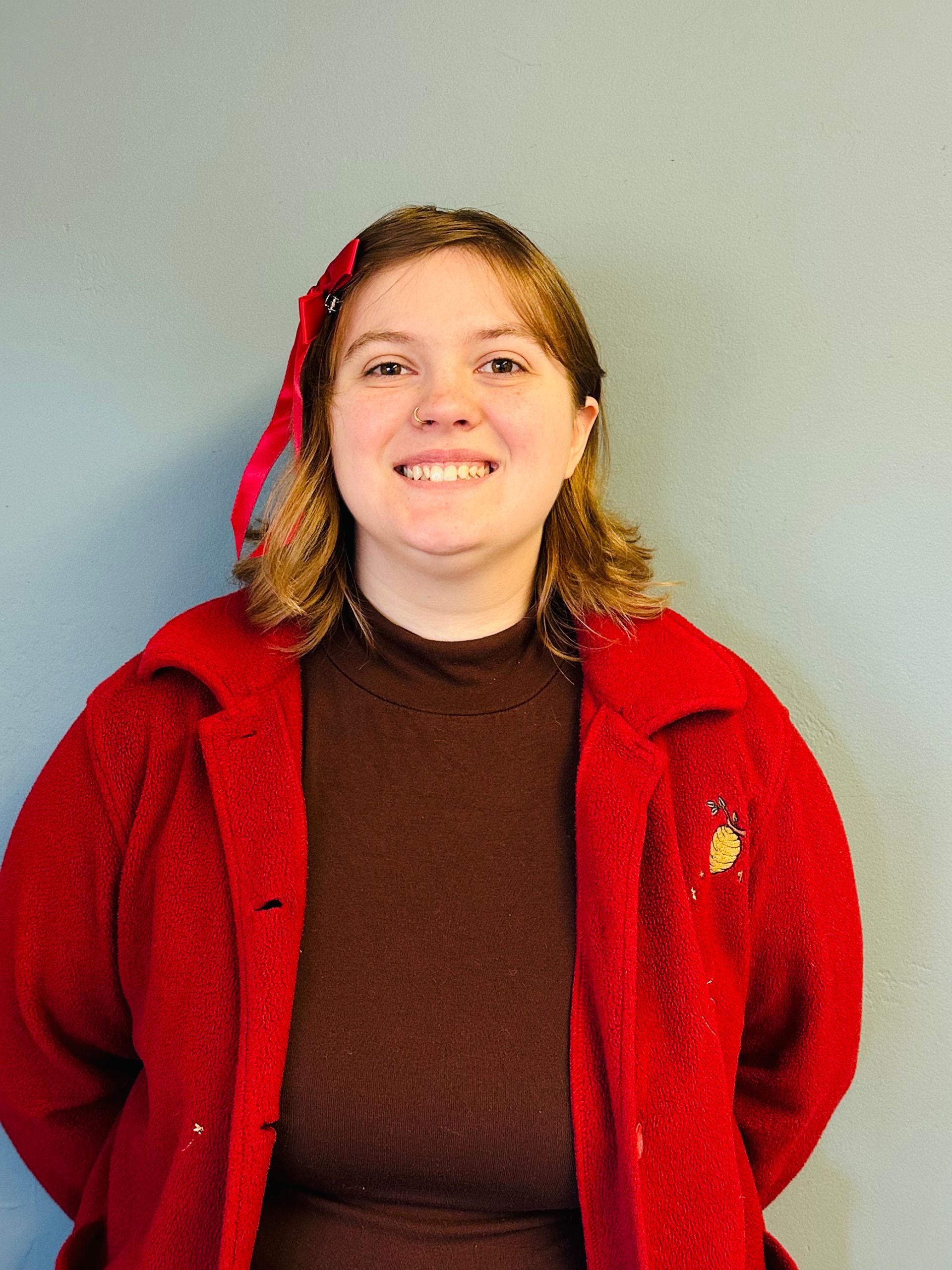 Smiling person in a red jacket against a plain gray background