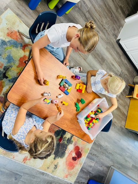 Three children playing with colorful blocks around a table on a rug in a living room