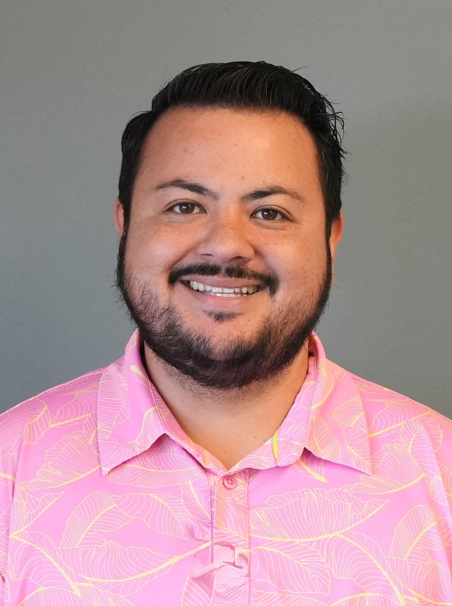 Smiling man in a pink patterned shirt against a gray background