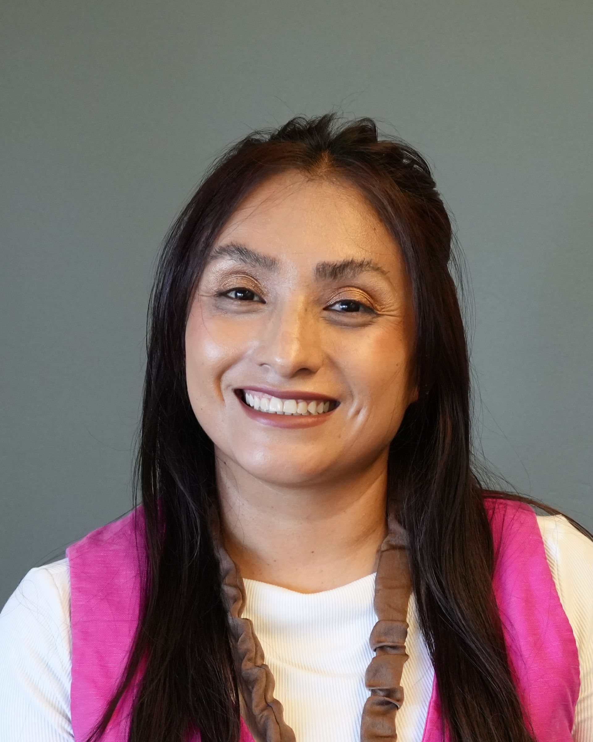 Smiling woman in a pink vest and white shirt against a gray background