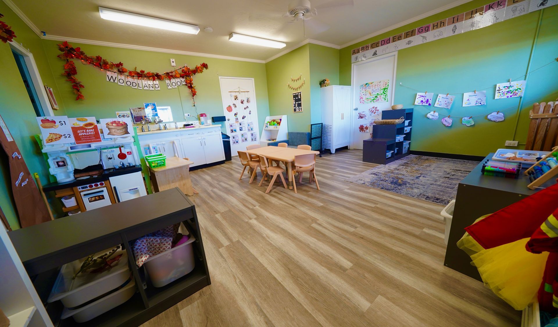 Colorful preschool classroom with small tables, wooden floor, wall decorations, and child-sized furniture