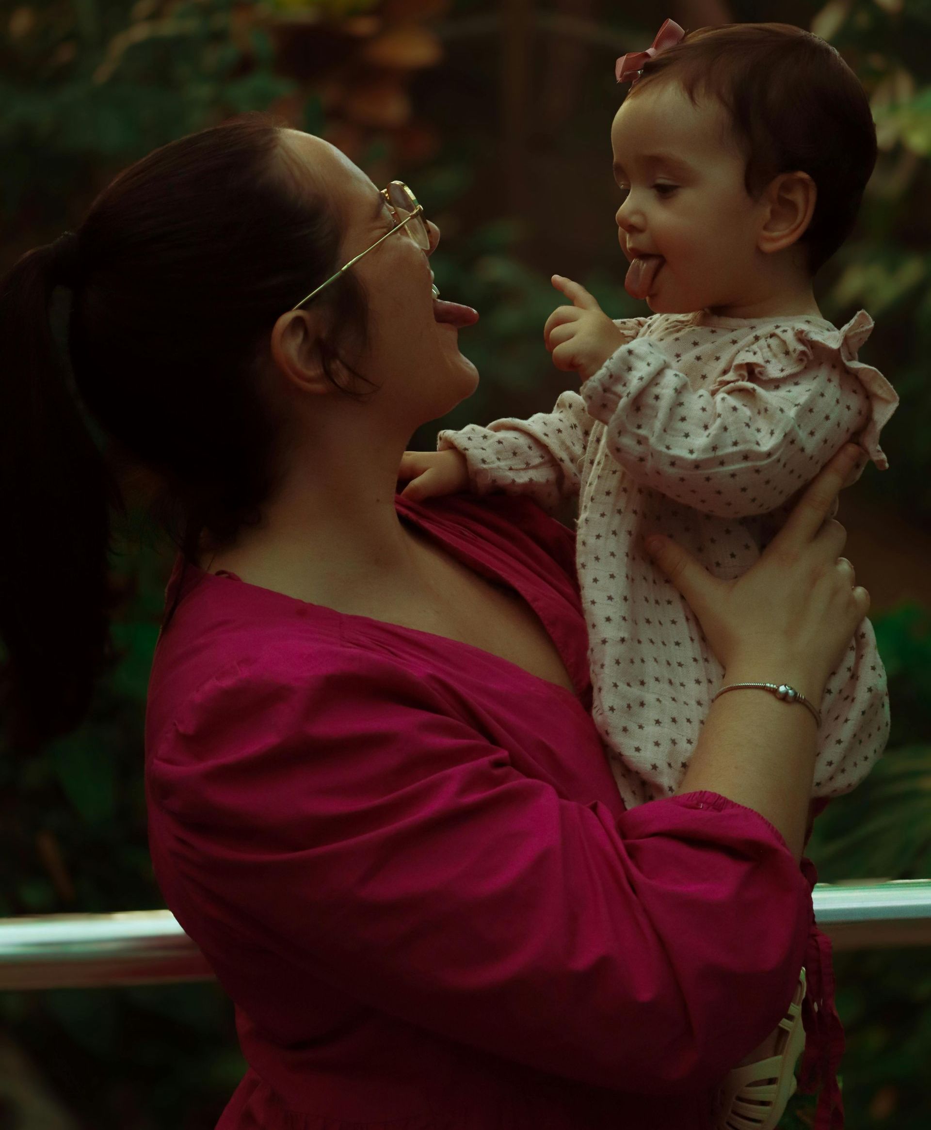 Woman in a pink top holding a smiling baby outdoors, facing each other lovingly.