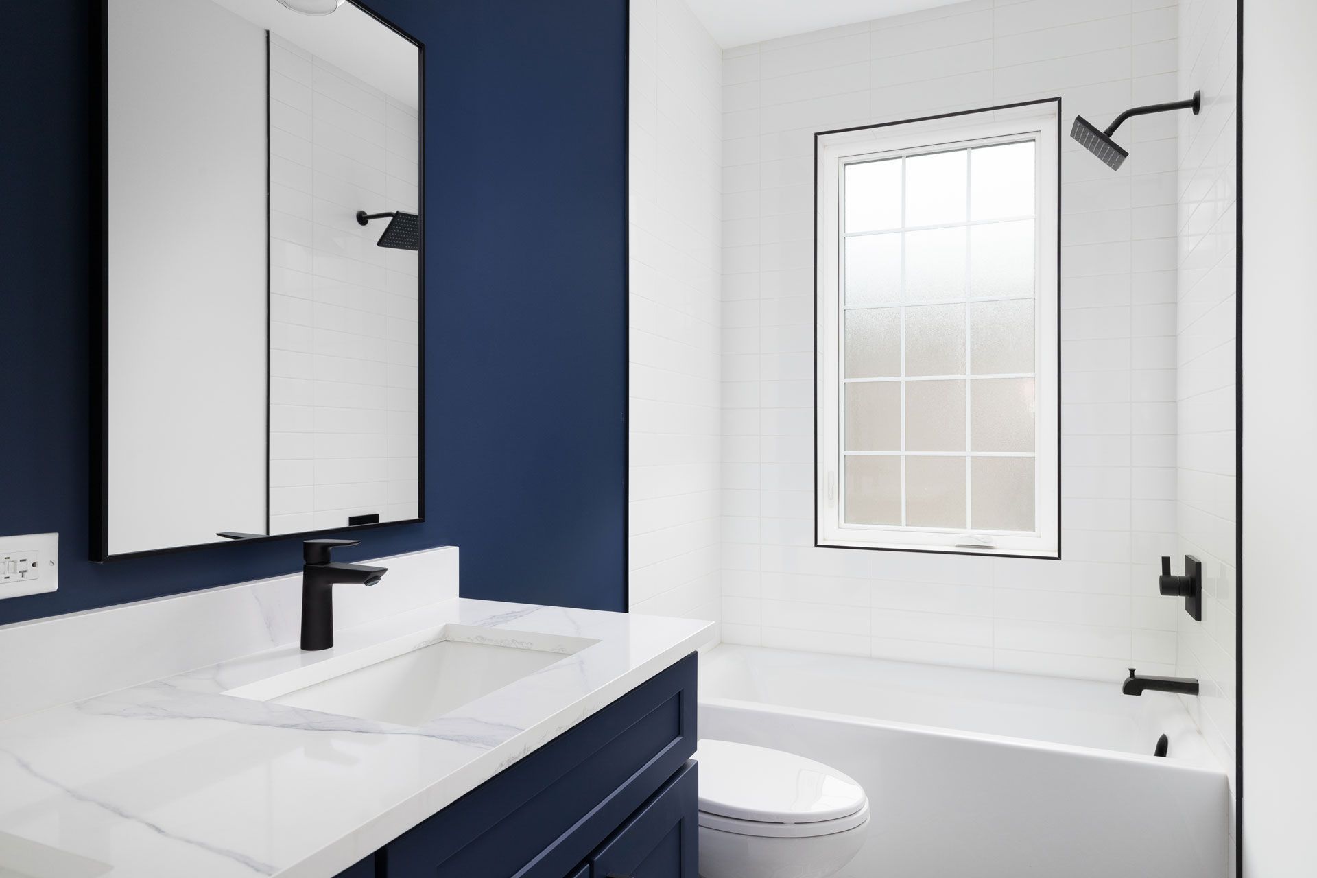 Navy blue and white bathroom with marble countertop, black fixtures, and a window.