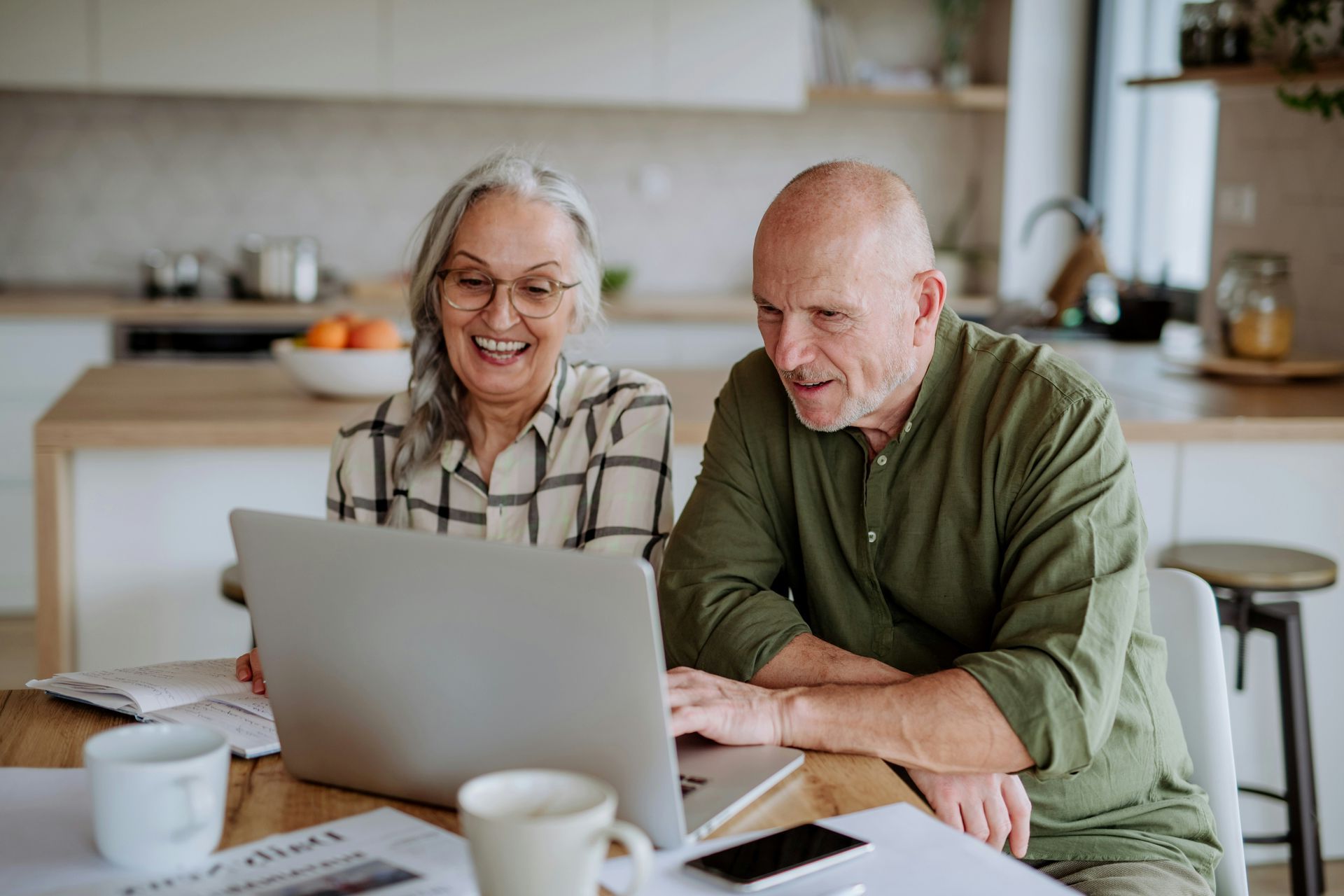 An elderly couple is sitting at a table looking at a laptop computer.