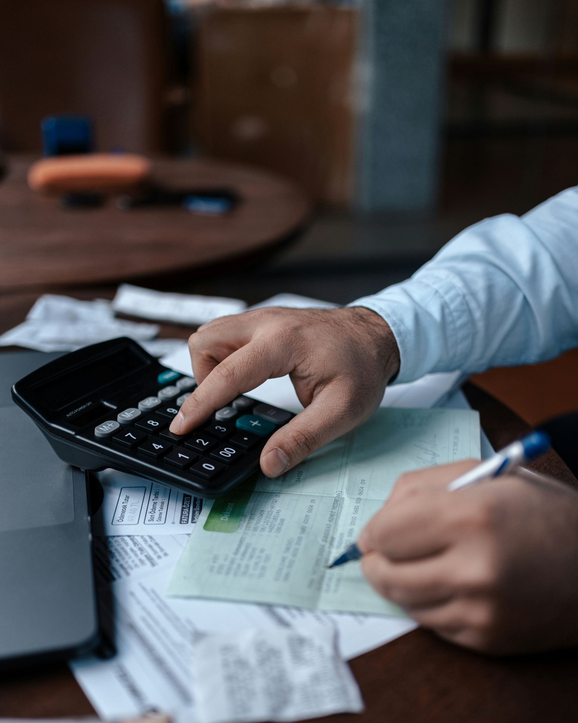 A man is using a calculator while writing on a piece of paper.