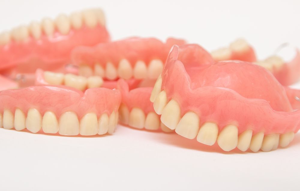 Close Up of a Bunch of Dentures on a White Surface — Cosmetic Denture Services–Jacob Maxwell in Mackay, QLD