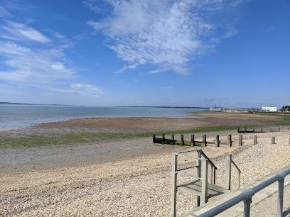 Sandy beach at low tide under a blue sky, with wooden steps and railings leading down to the shore.