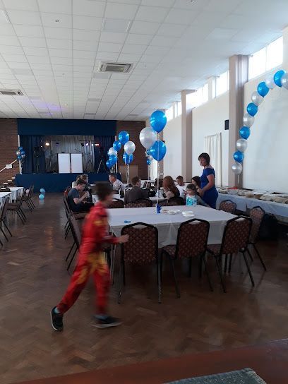 Decorated banquet hall with blue balloons, tables, and children seated; one child runs in the foreground