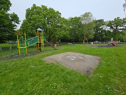 Empty playground with green climbing structure, slide, and grassy field under trees