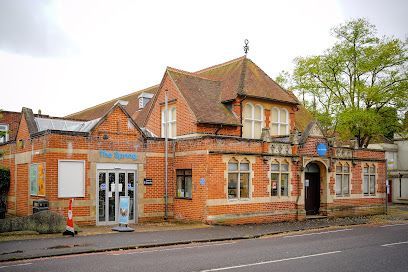 Brick building with red tiled roofs and a storefront on a street, under cloudy skies