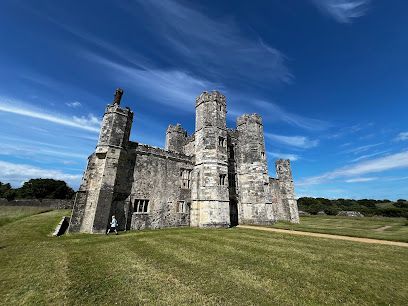 Stone castle ruins on a grassy hill beneath a bright blue sky with wispy clouds