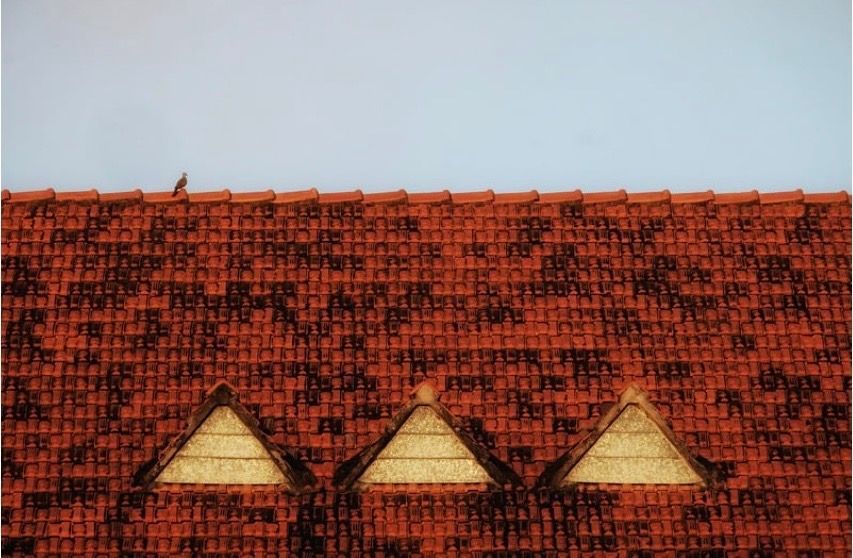 Red tiled roof with three small triangular dormer windows under a pale blue sky