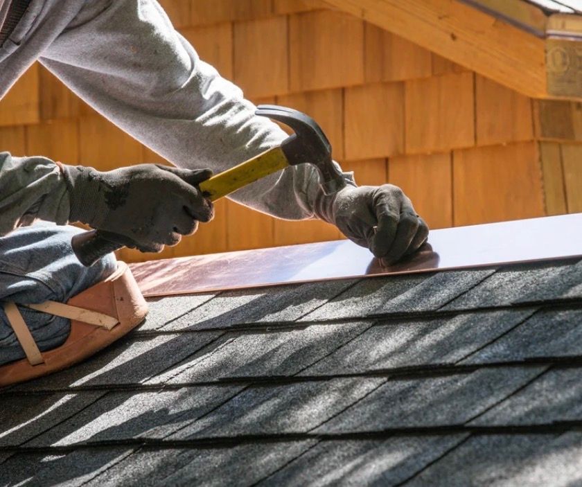 Workers installing roof shingles with a hammer on a house roof under construction