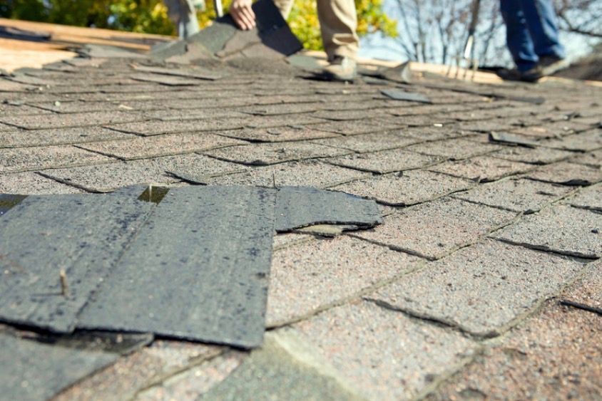 Close-up of damaged roof shingles with people standing in the background