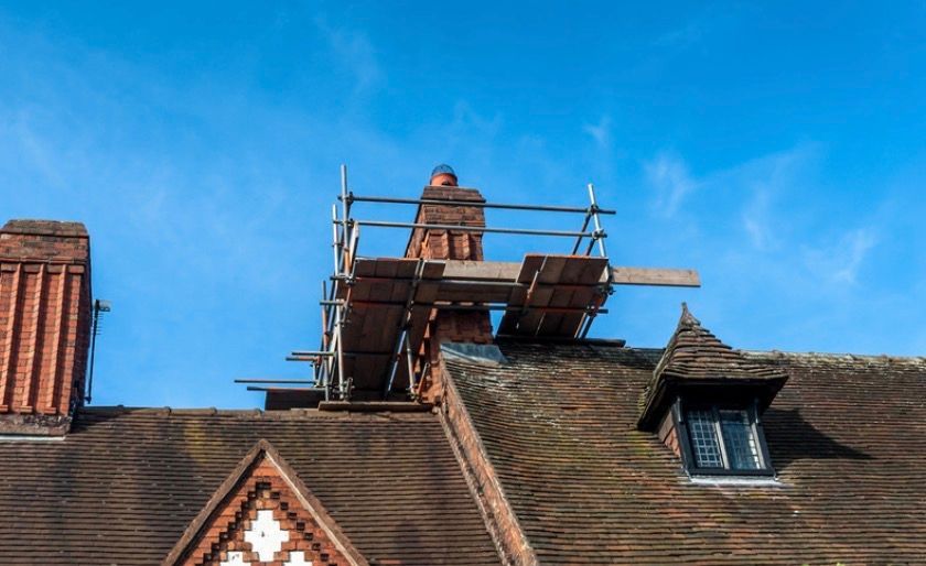 Roofer working on a scaffold atop a brick building under a bright blue sky