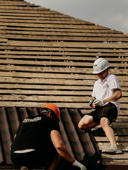 Two workers on a roof, one in a white hard hat, installing corrugated roofing panels