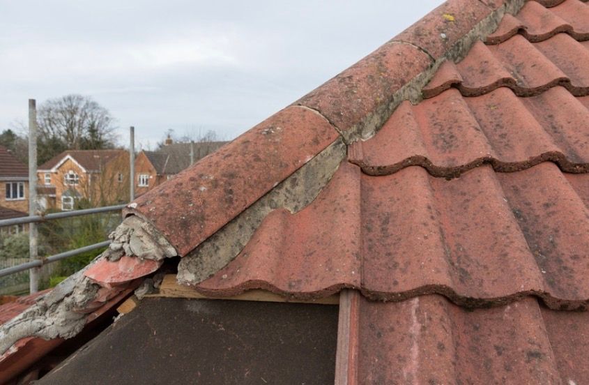 Damaged red roof tiles with a cracked ridge on a house roof