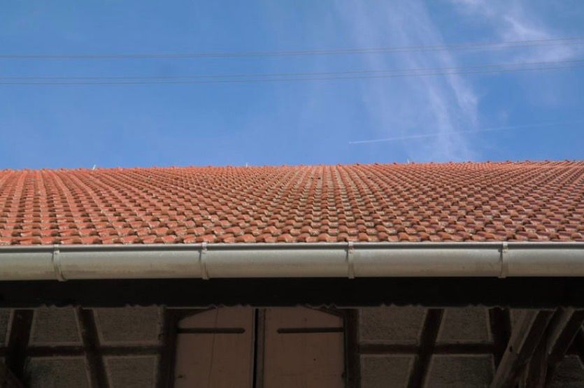 Red tiled roof with white gutter beneath a blue sky with thin clouds
