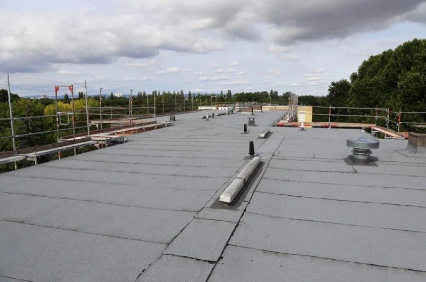 Rooftop under construction with gray membrane panels, railings, vents, and a cloudy sky.