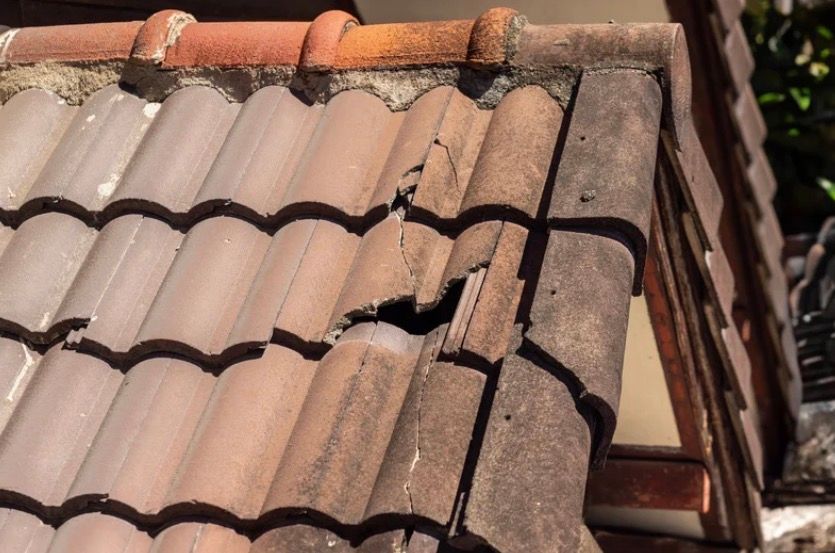 Damaged terracotta roof tiles with a broken section exposing the underlayment