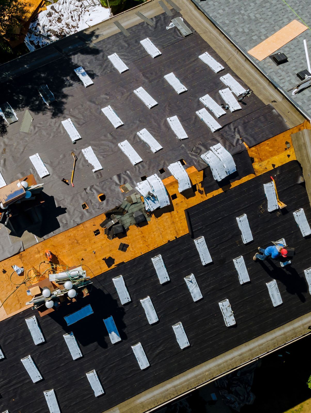 Aerial view of rooftop workers on a black roof with a bright orange safety walkway