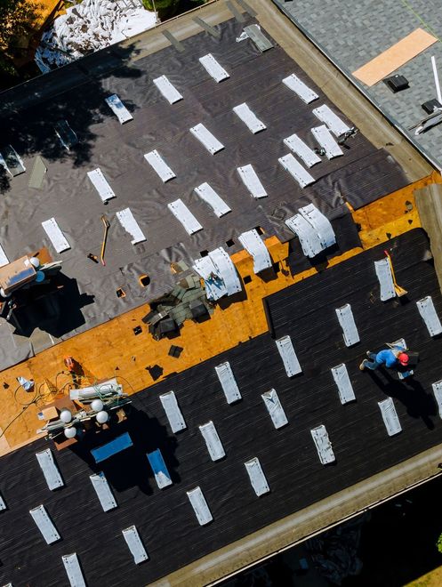 Aerial view of rooftop workers on a black roof with a bright orange safety walkway