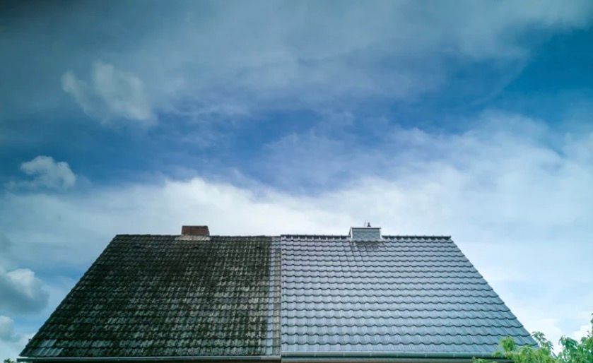 Blue sky with wispy clouds above two adjacent rooftops, one dark green and one light gray.