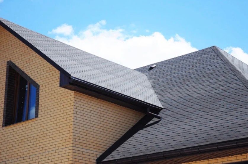 Brick house roofs with dark gray shingles against a blue sky