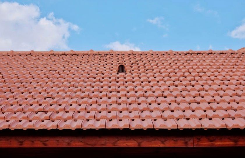 Red clay roof tiles against a blue sky with a small vent opening