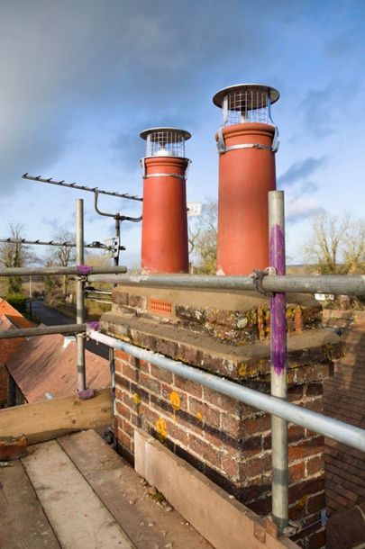 Two red chimney stacks on a brick rooftop under a blue sky