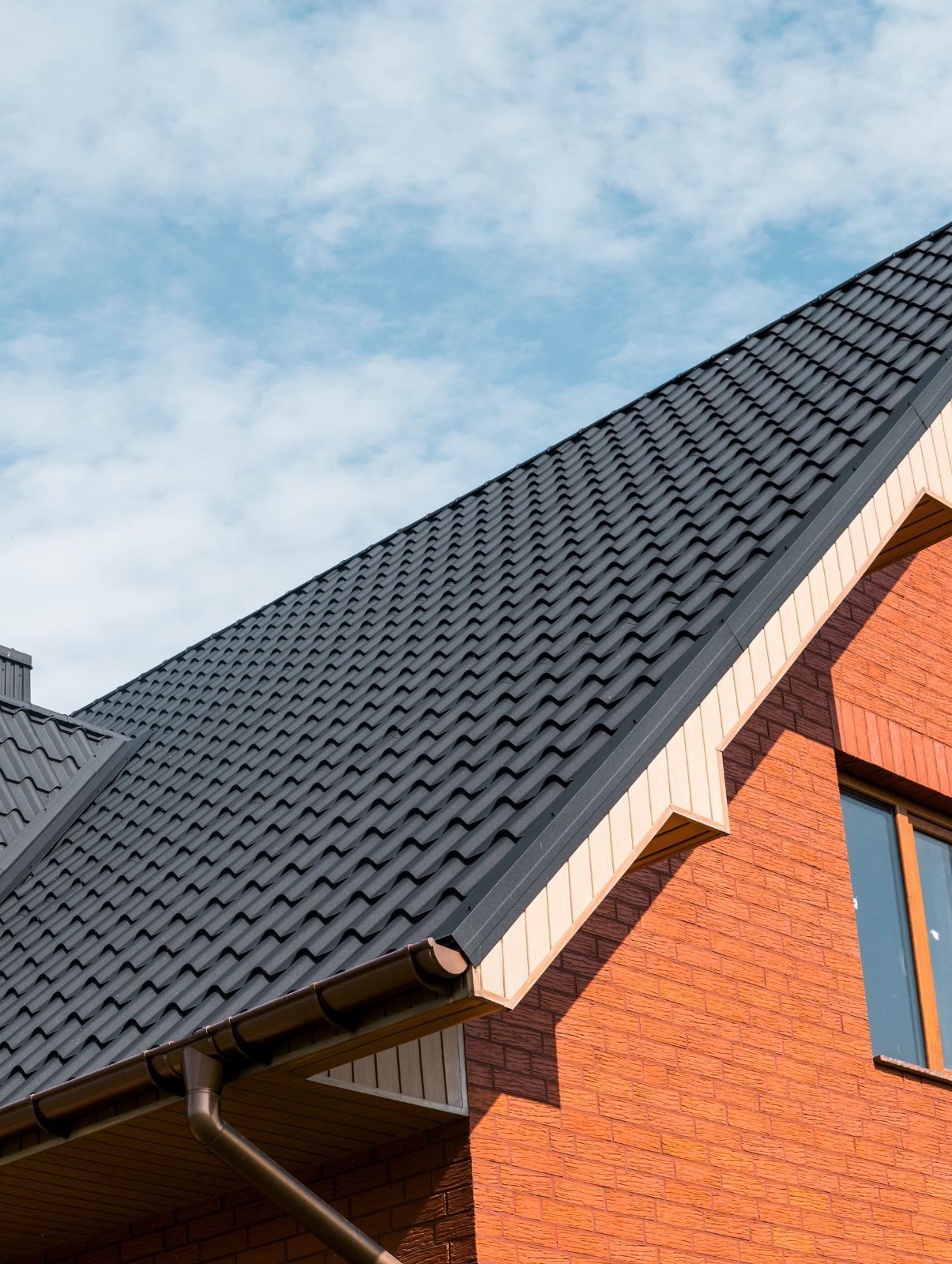 Dark gray tiled roof on a red brick house against a partly cloudy sky