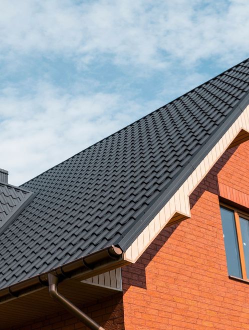 Dark gray tiled roof on a red brick house against a partly cloudy sky