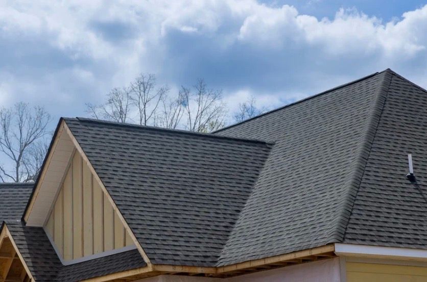 Gray shingled house roof with gables against a cloudy sky
