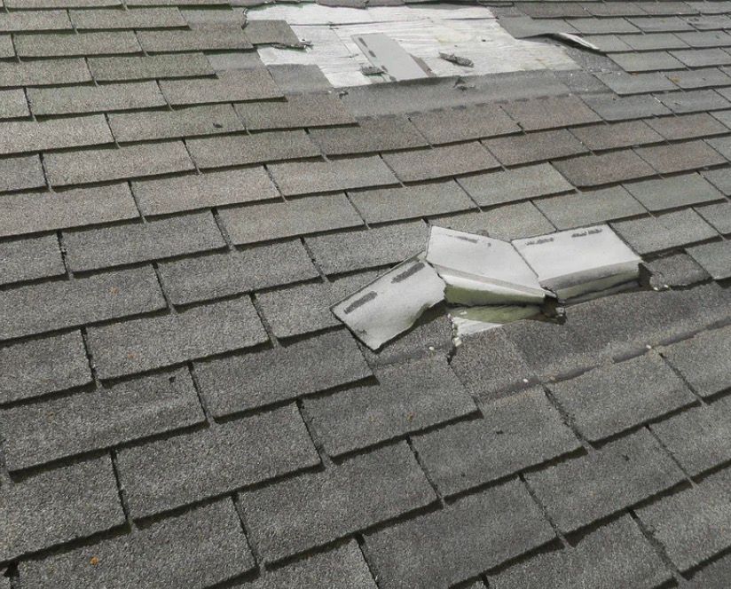 Damaged shingle roof with torn, lifted pieces and debris scattered on the gray surface
