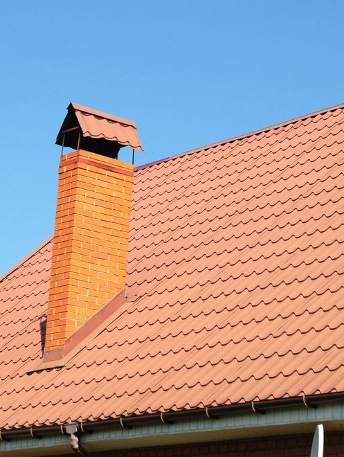 Red tiled roof with a brick chimney against a blue sky