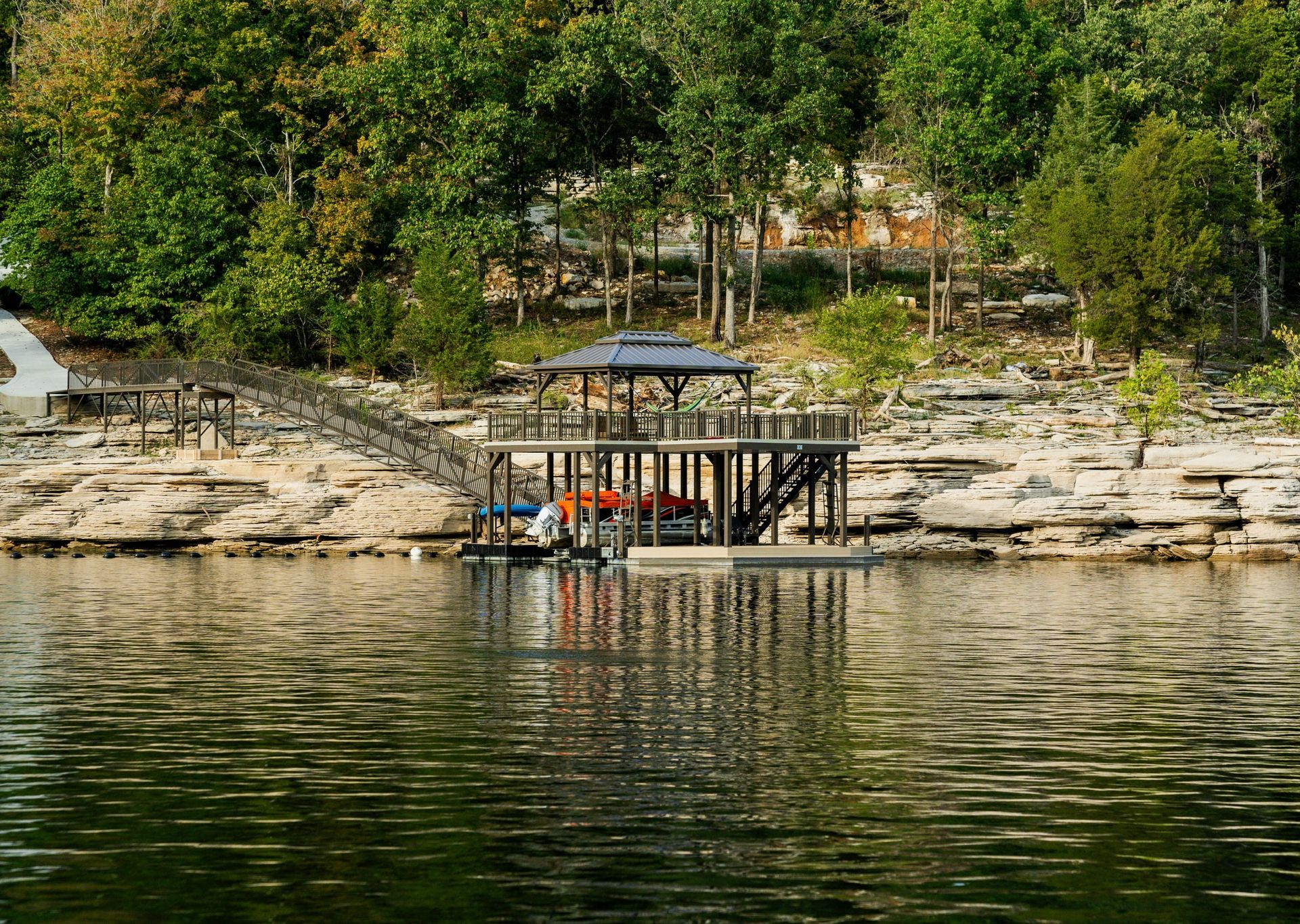 Small dock with boats on a rocky lakeshore, backed by green trees and a hillside