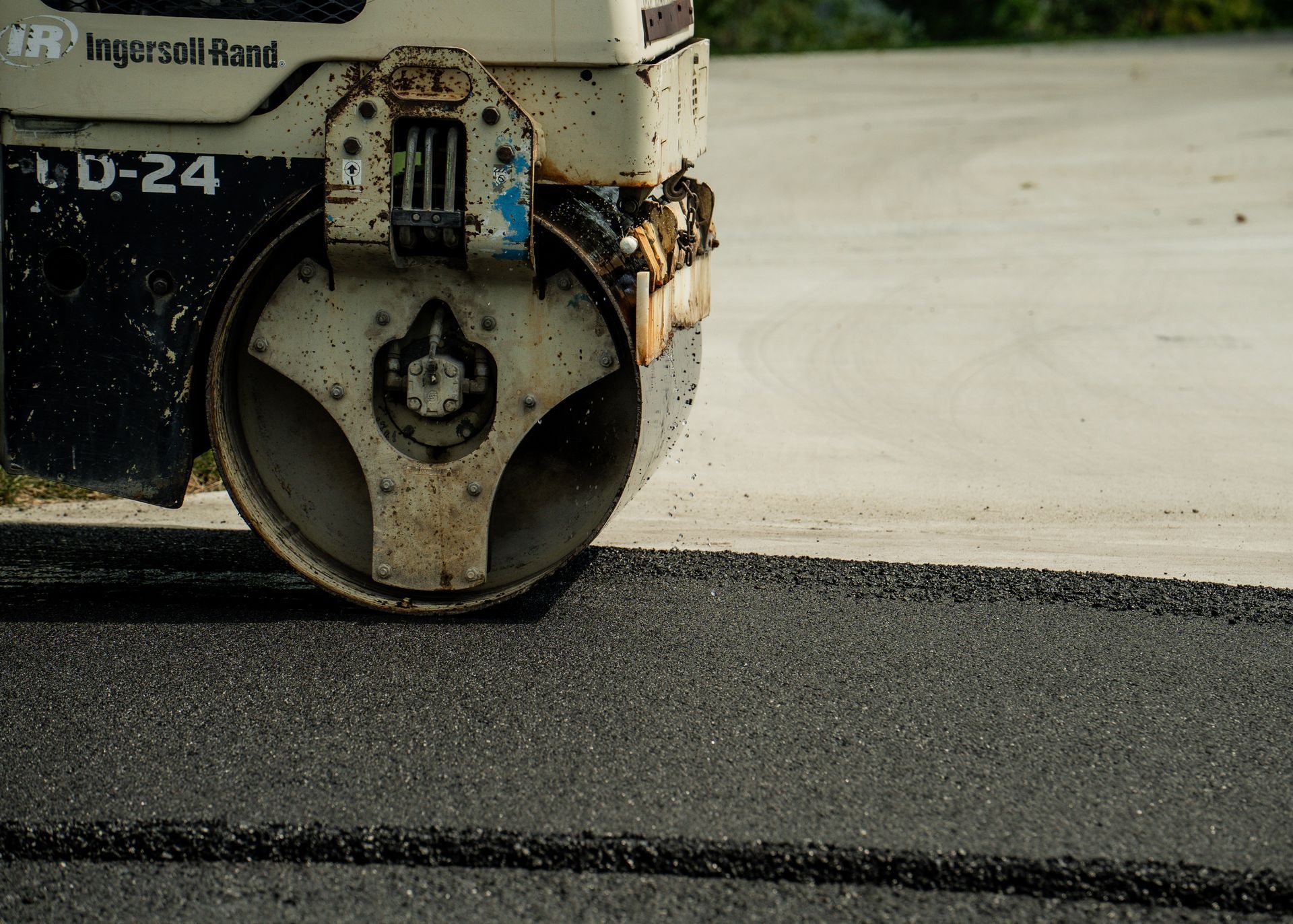 Road roller compacting fresh black asphalt on a paved surface