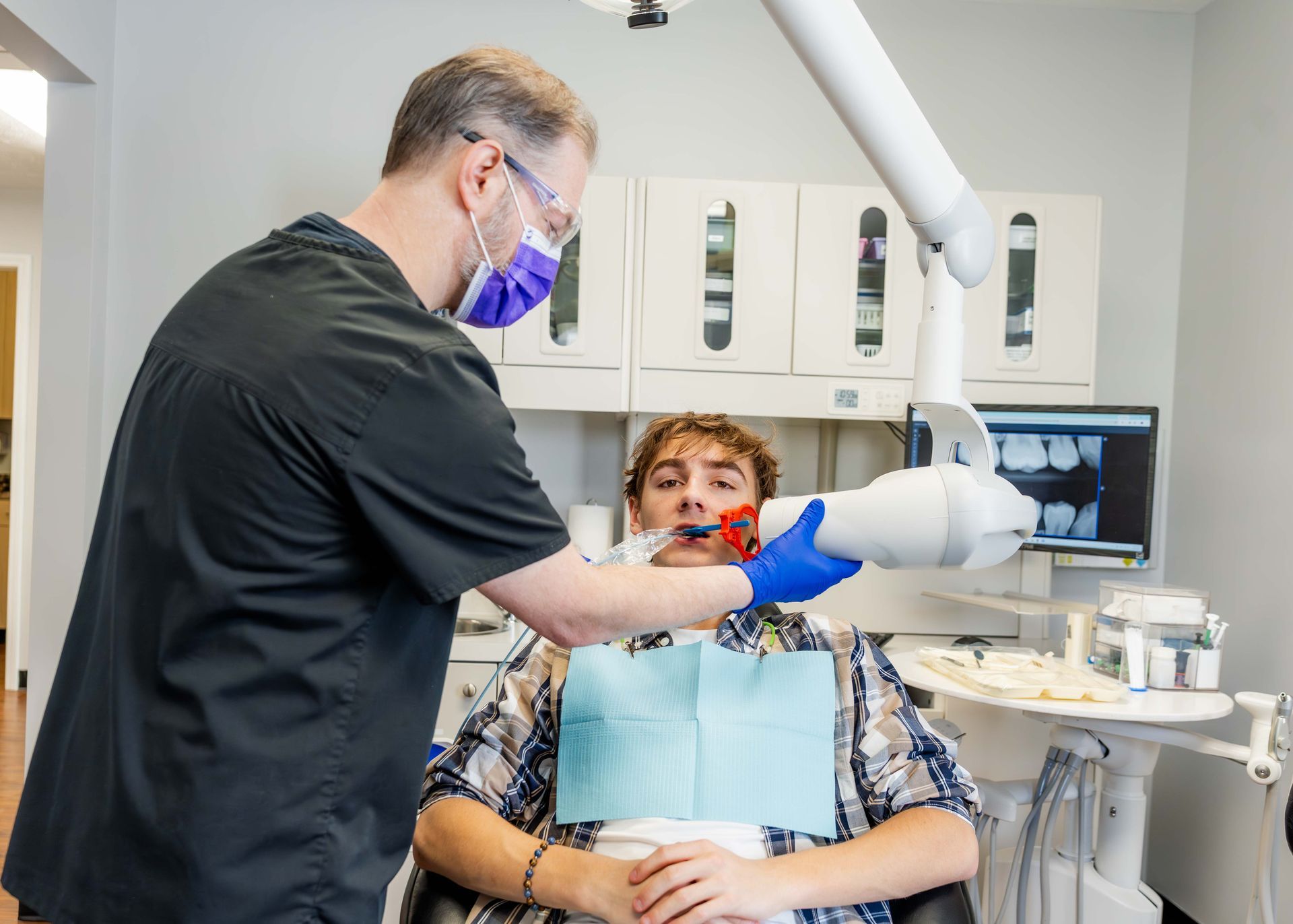 Dentist wearing gloves adjusts equipment while seated patient opens mouth in a dental clinic