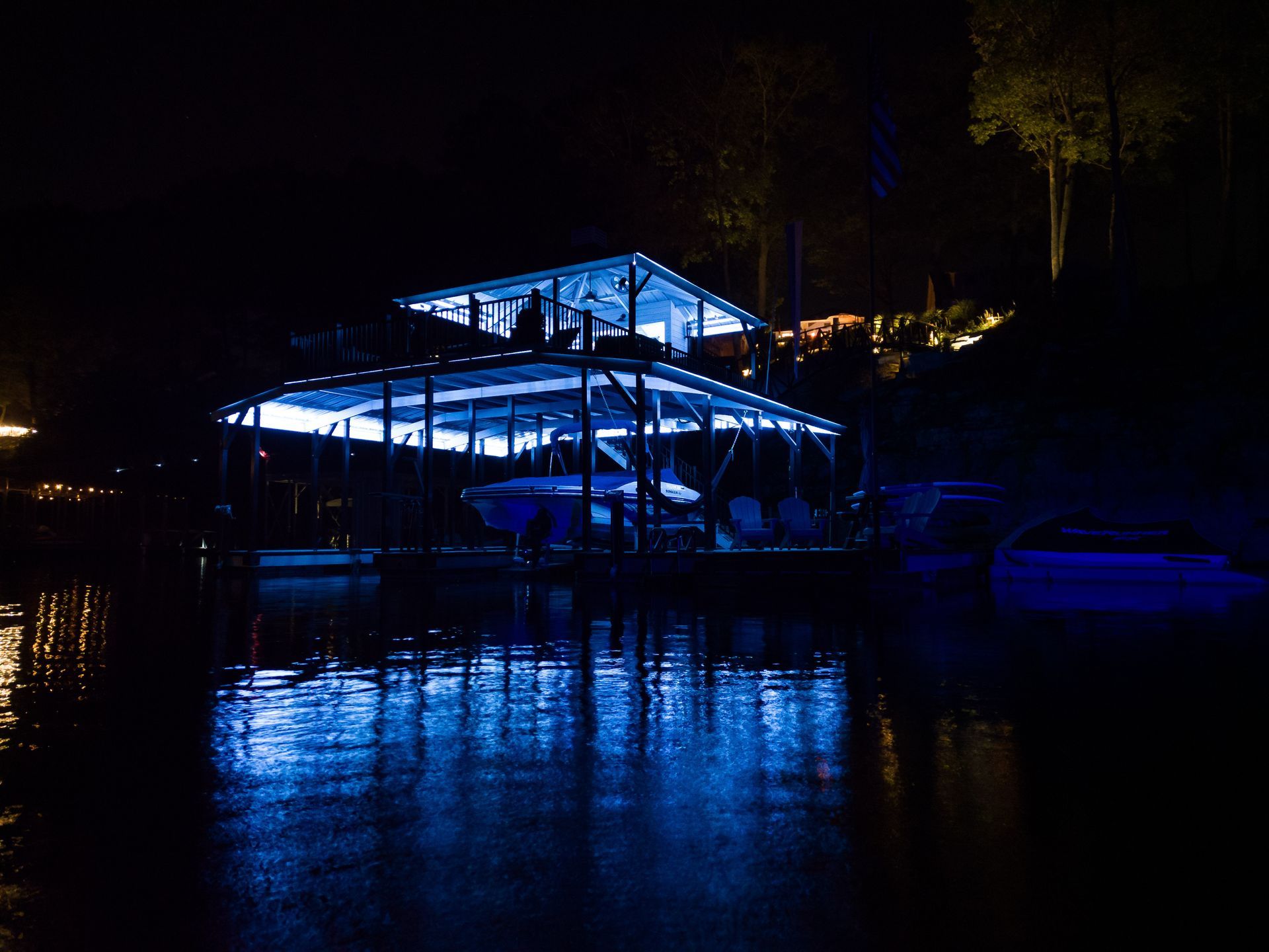 Blue-lit boathouse at night reflecting on calm water