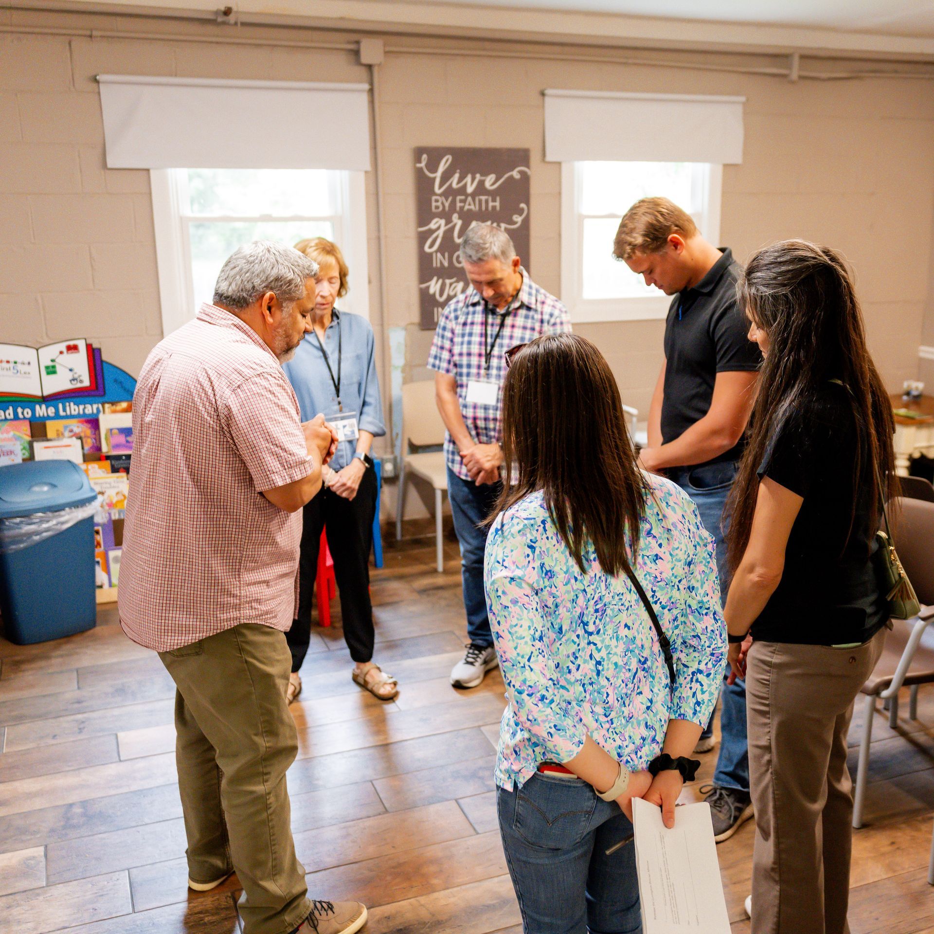 People gathered in a room, standing in a circle and looking down at papers during a small meeting.