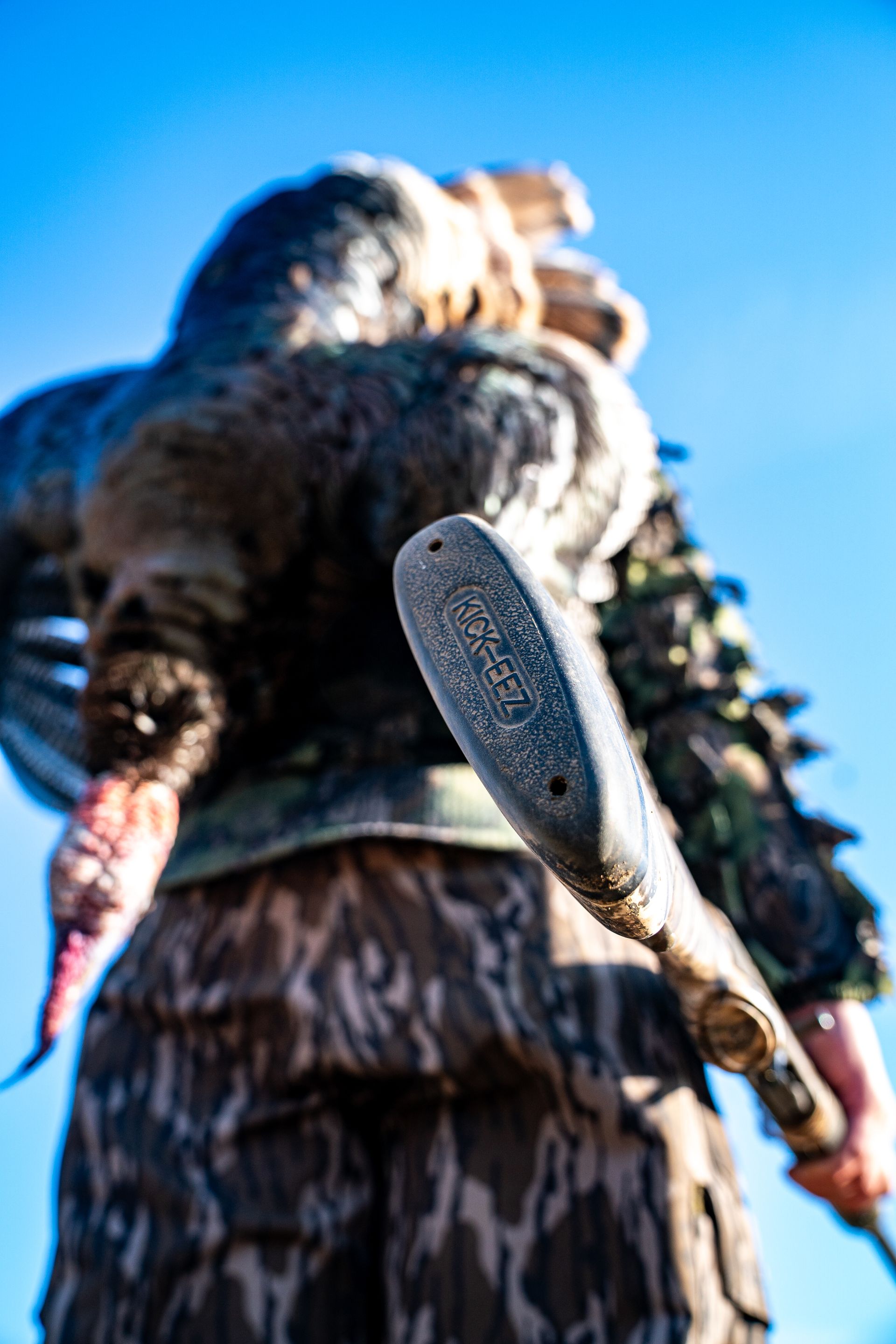 Low-angle view of a person in camouflage clothing carrying a rifle against a blue sky