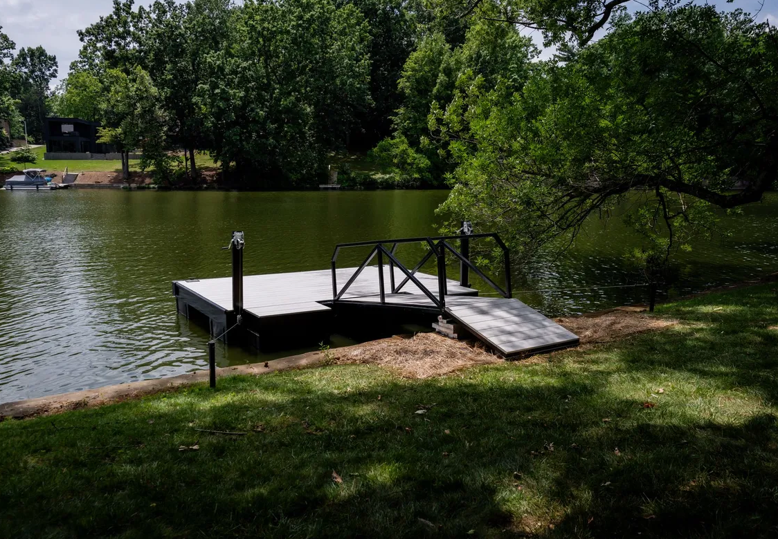 Small dock with ramp extending into a calm lake, surrounded by green trees and grass