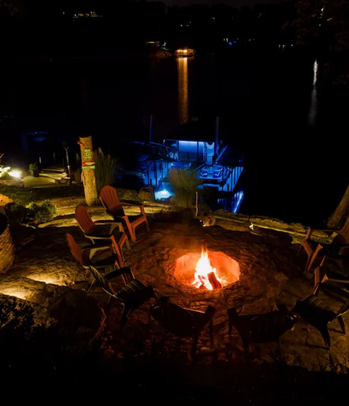 Nighttime lakeside fire pit with Adirondack chairs and blue-lit dock seating