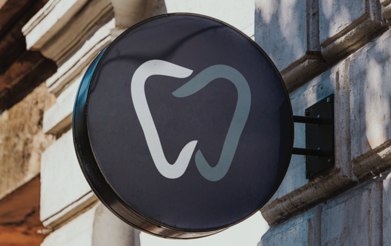 Dental clinic sign with a white tooth icon on a dark round plaque mounted on a brick wall