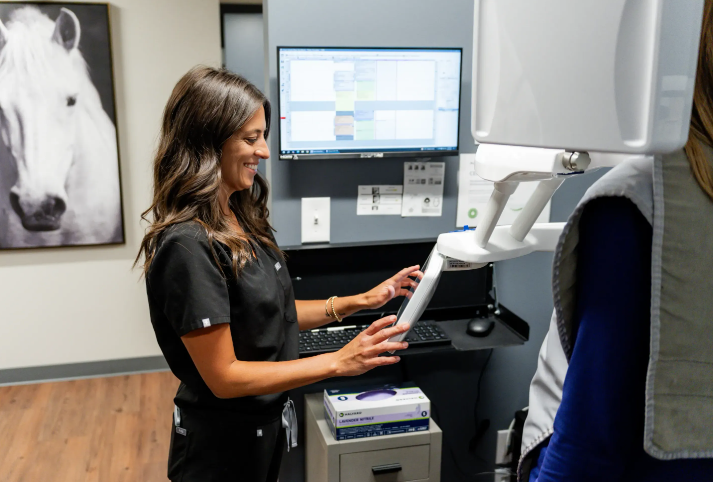Technician operating a medical imaging machine beside a horse photo in a clinic room