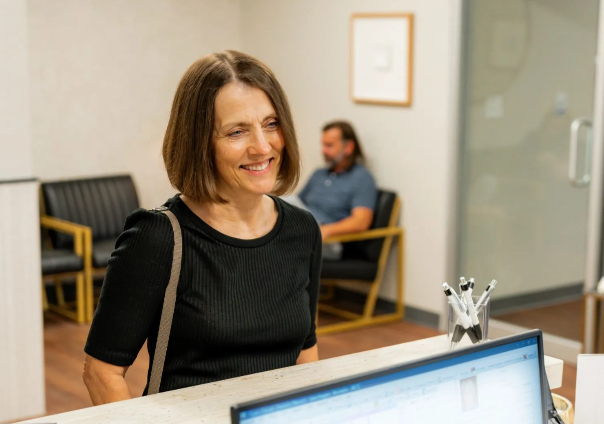 Smiling woman at an office reception desk with a computer in the foreground