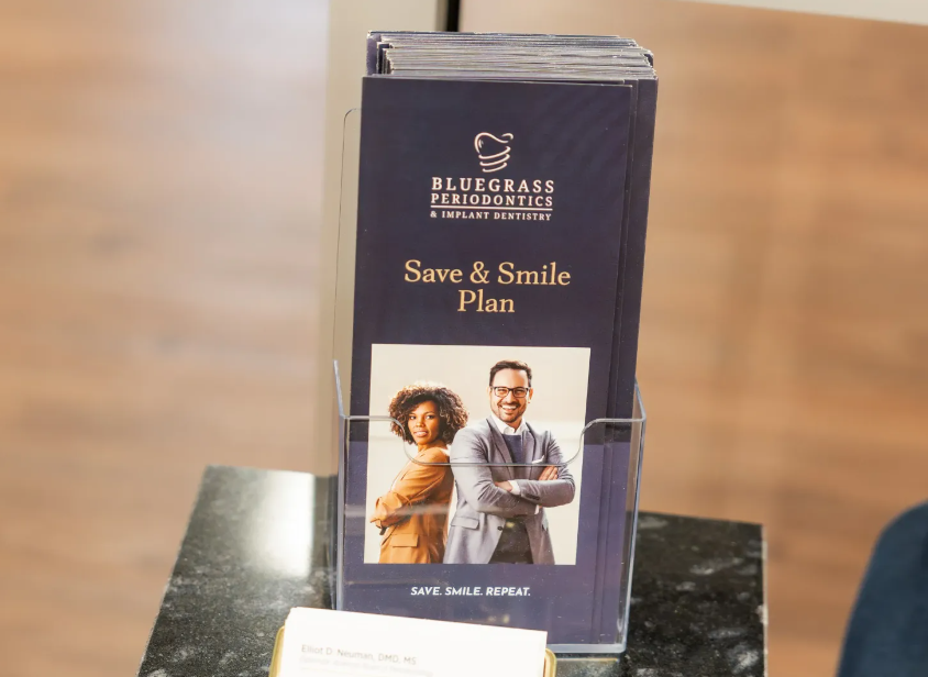 Blue brochure stand for Bluegrass Family Savings “Save & Smile Plan” on a table outdoors.