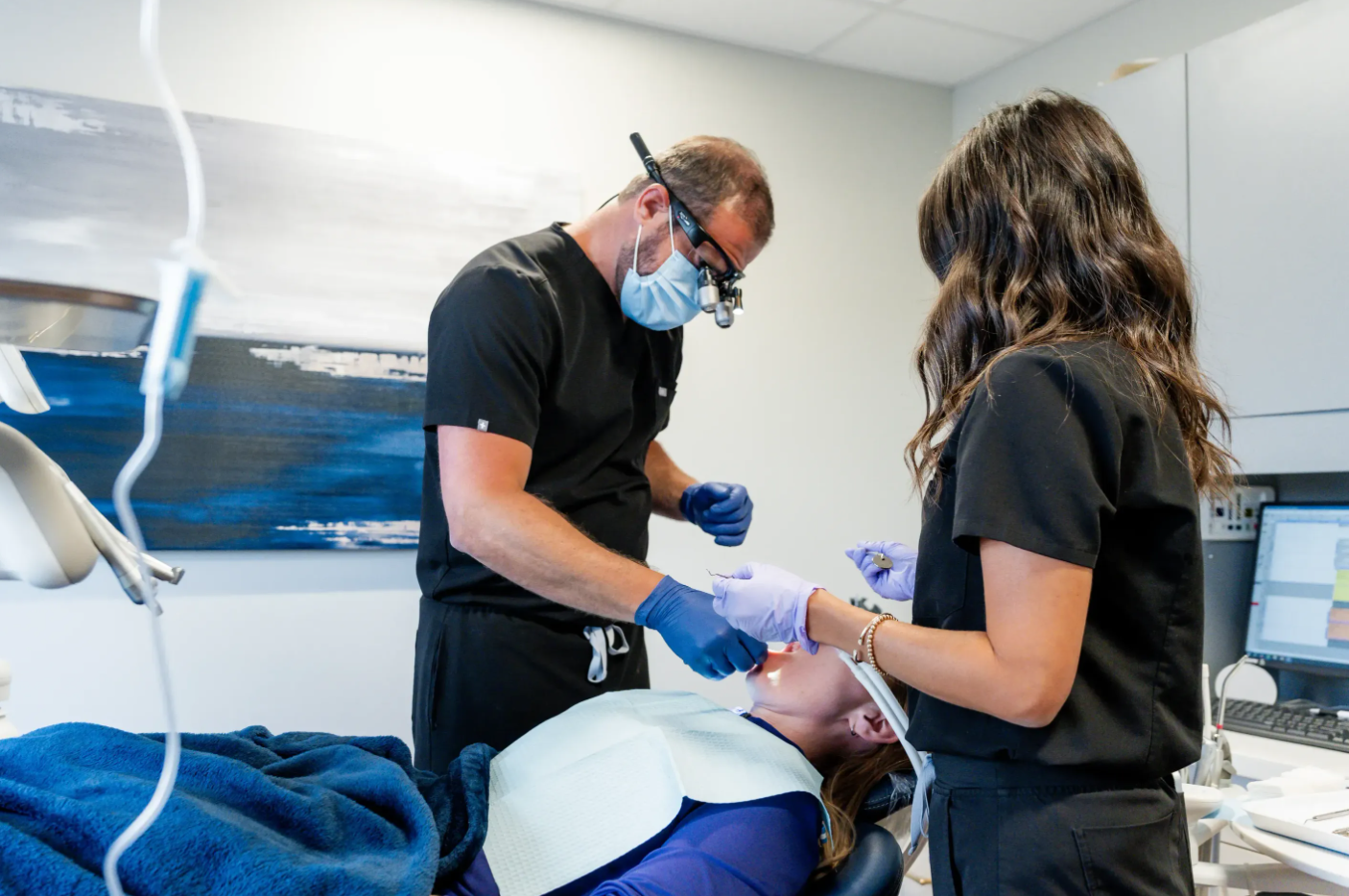Dentist examining a patient while an assistant holds tools in a bright dental clinic
